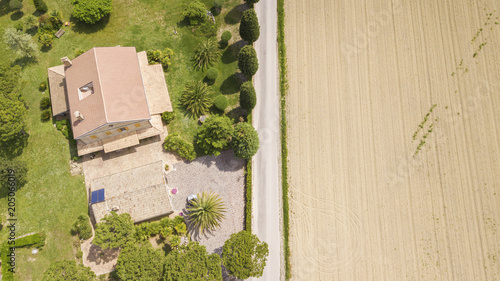 Perpendicular aerial view of a road passing near a villa and cuts through the fields of agriculture. On one side a grain camo from the other a villa with private parking.