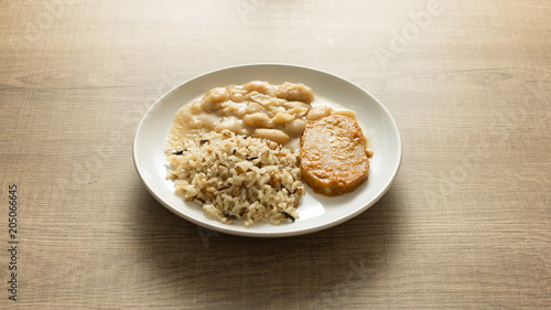 Pork chop, Brown rice and white beans. White dish on wooden table.