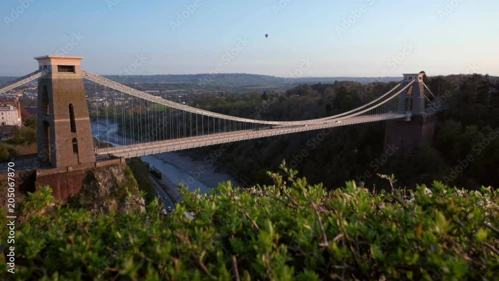 Camera rises jib style from behind fence to reveal Clifton Suspension Bridge in Avon England. Shot on spring evening with a hot air ballon in the sky Camera rises jib style from behind fence to reveal Clifton Suspension Bridge in Avon England. Shot on spring evening with a hot air ballon in the sky