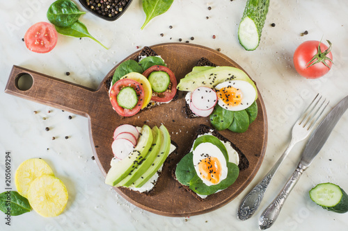 Summer sandwiches with fresh vegetables, eggs, avocado, tomato, rye bread on light marble table. Top vew. Appetizer for party. Flat lay.