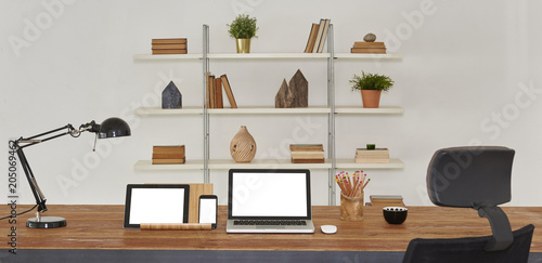 Open laptop with digital tablet and white smartphone. All with isolated screen on old wooden desk. Bookcase background office interior.