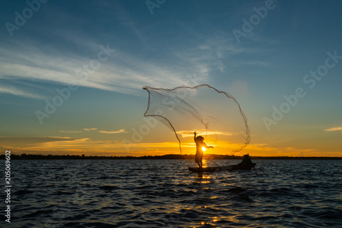 Foto Un-identified silhouette fisher man on boat fishing by throwing fishing net