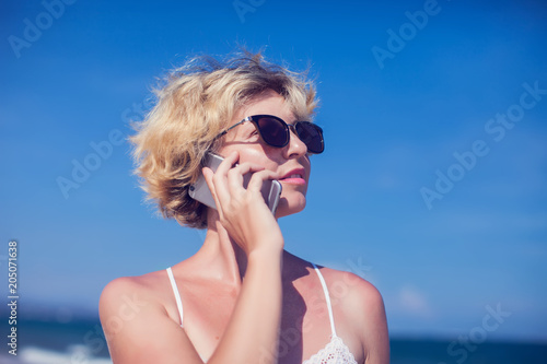 Young happy woman talking on mobile phone on a beach with sea background