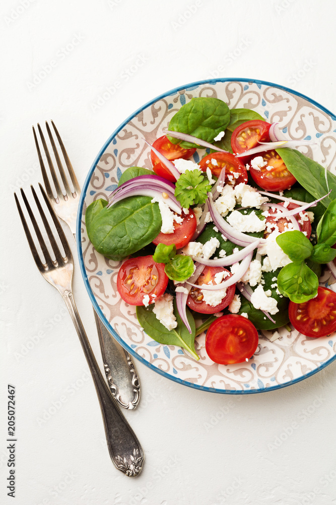Tomatoes, spinach leaves, red onions and feta cheese salad on a light ceramic plate. Selective focus. Top view. Tomatoes, spinach leaves, red onions and feta cheese salad on a light ceramic plate. Selective focus. Top view.