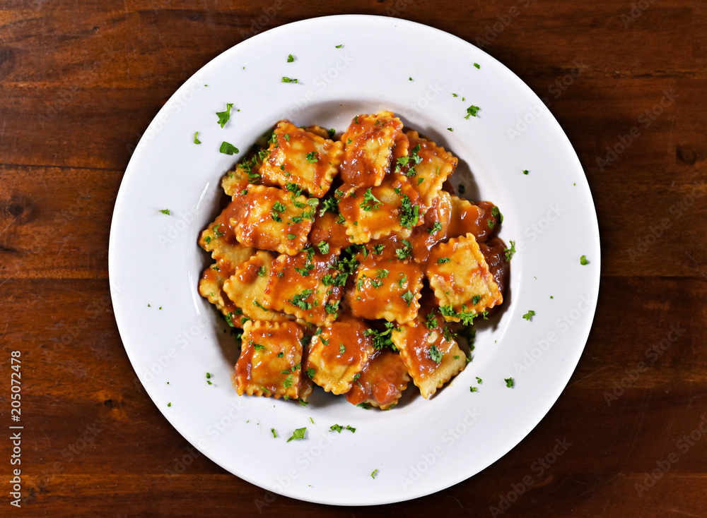 Fresh ravioli pasta with parsley and basil leaf, italian cuisine. White plate and wooden table, pasta dish.