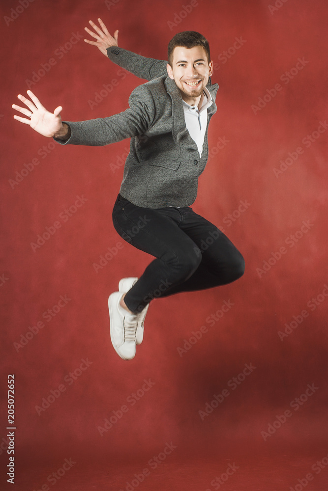 Photo of a young man on a red wall background looking at camera jumping.