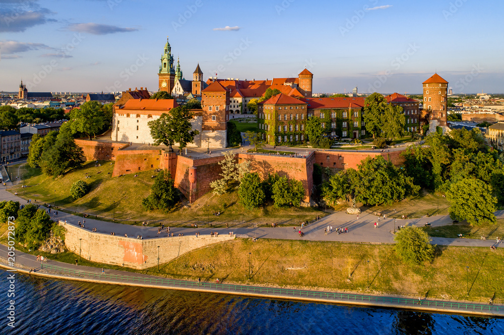 Krakow, Poland. Wawel Hill, royal Cathedral and castle. Aerial view in sunset light. Vistula River and far view of St. Mary (Mariacki) church on the left. Riverbank with promenade and walking people Krakow, Poland. Wawel Hill, royal Cathedral and castle. Aerial view in sunset light. Vistula River and far view of St. Mary (Mariacki) church on the left. Riverbank with promenade and walking people