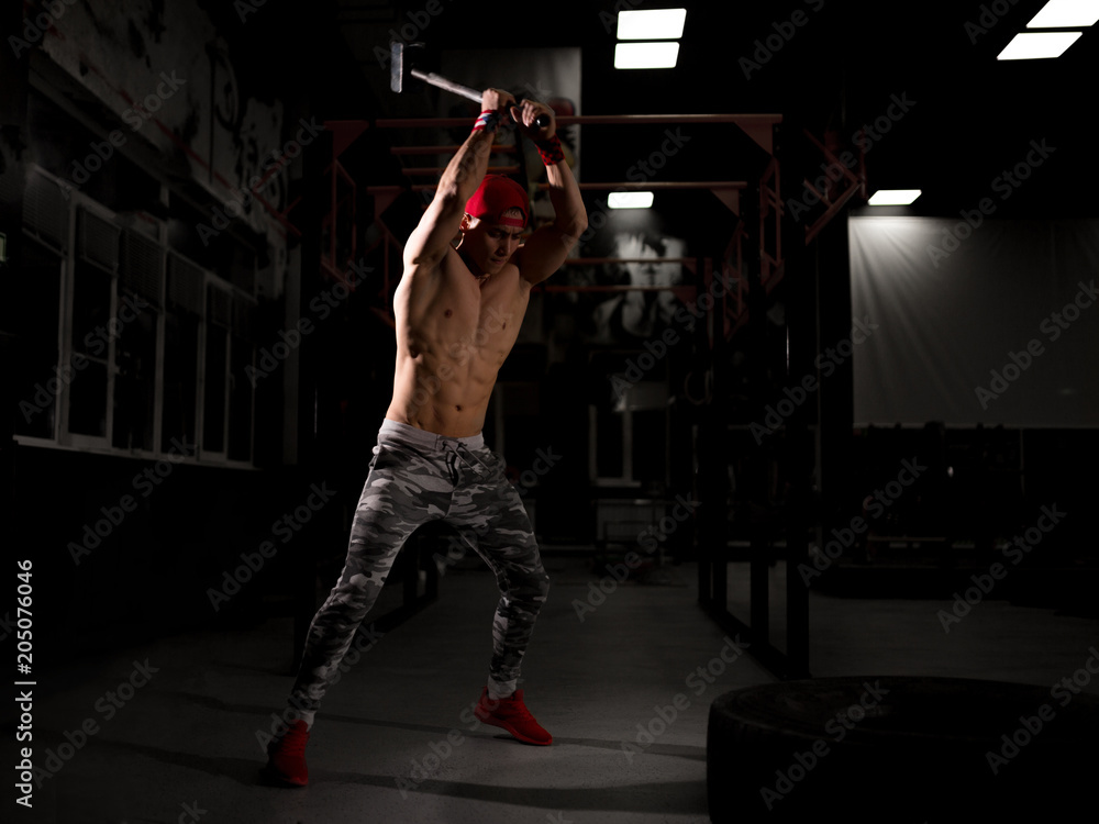A young sportsman in a red cap in the gym. Do exercises with a hammer. Crossfit training in the gym. A young sportsman in a red cap in the gym. Do exercises with a hammer. Crossfit training in the gym.