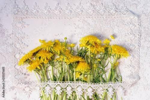 Fototapeta Naklejka Na Ścianę i Meble -  bouquet of wildflowers, dandelions and buttercups, in the style of a rustic postcard on a white textured cement background in a picture frame made of lace. copy space for your greeting text.