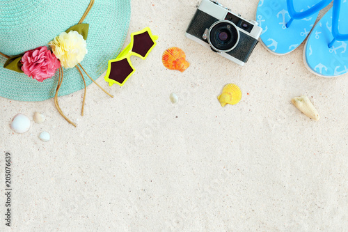 Beach background.  Top view of beach sand with straw hat, sunglasses, shells, camera, slippers and coral.  Summer background concept.