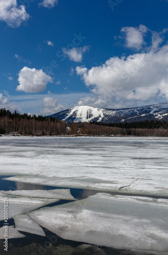 spring lake with cracked ice floes on the background of the ski resort and the blue sky with clouds. the vertical location of the frame