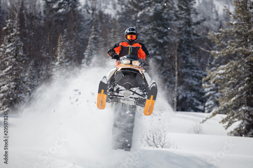 guy on a snowmobile in a jump on the background of the winter forest. a bright suit and a snowmobile, front view, caterpillar, snow spray