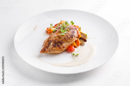 Grilled chicken breast with vegetables. Served on a white plate