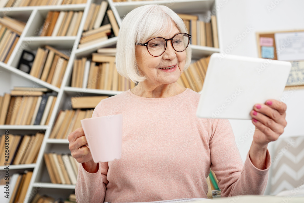 New facts. Enthusiastic senior woman using tablet while enjoying tea New facts. Enthusiastic senior woman using tablet while enjoying tea