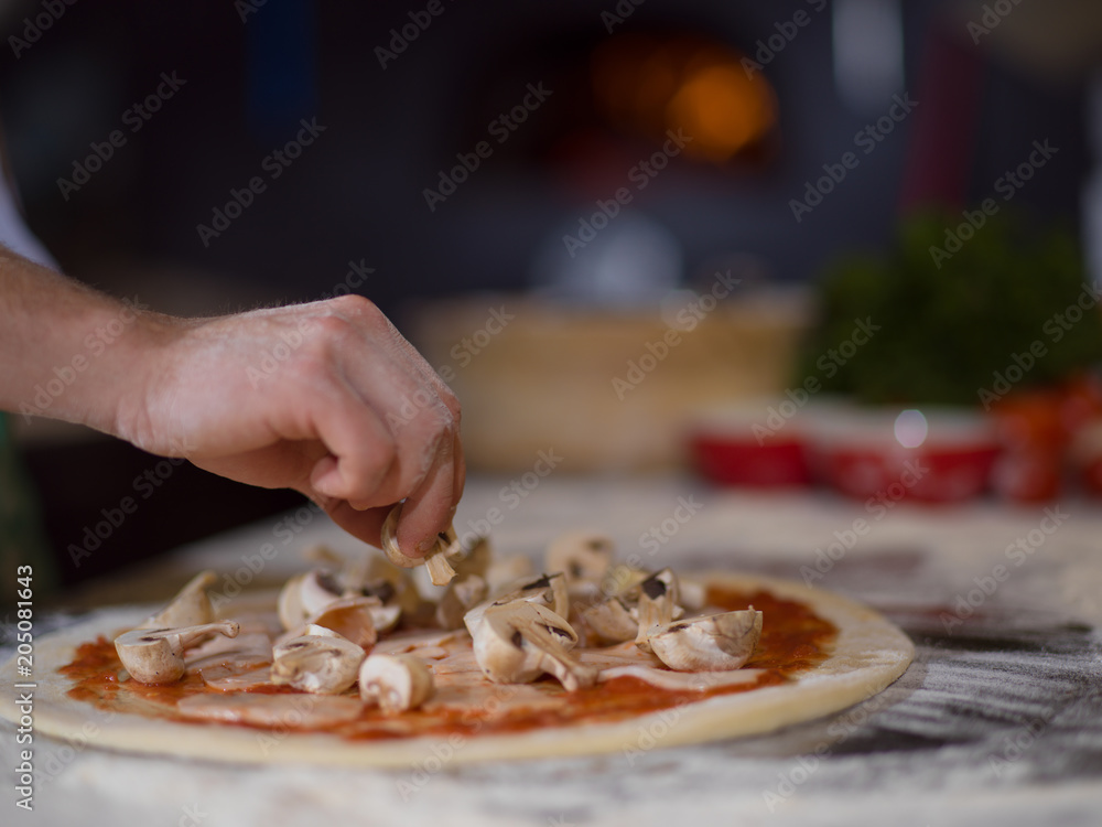 chef putting fresh mushrooms on pizza dough