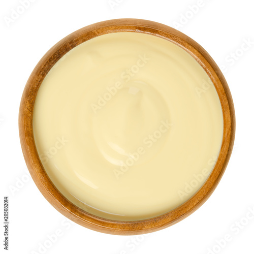 Sauce Hollandaise in wooden bowl. Also Dutch sauce. Emulsion of egg yolk, butter, water and lemon juice. Eaten with steamed vegetables or Eggs Benedict. Macro food photo close up from above over white