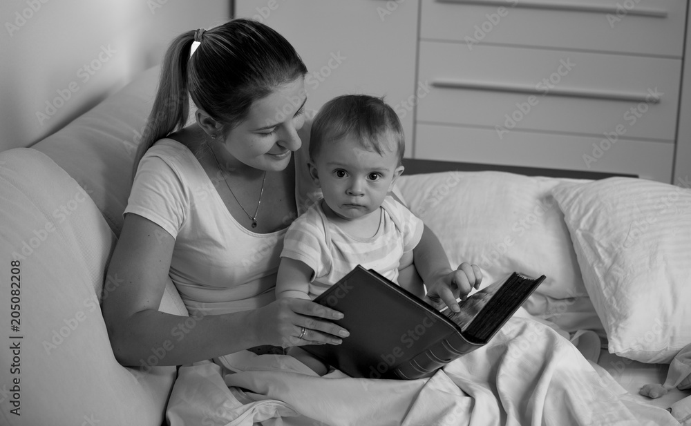 Black adn white portrait of mother with baby lying in bed and reading book Black adn white portrait of mother with baby lying in bed and reading book