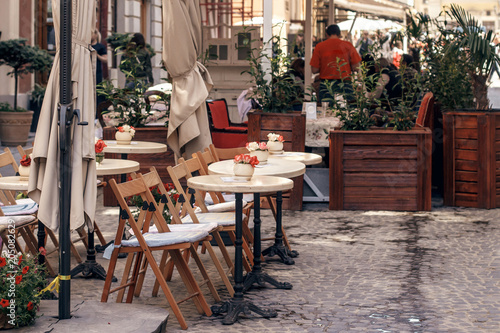 beautiful cafe terrace with little vintage tables and wooden chairs and plants  modern exterior of restaurant in european city street. food court in old city