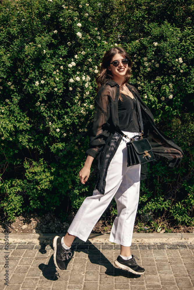 beautiful Stylish Hipster Girl with beautiful hair walking at floral bushes in sunny day. Gorgeous Boho Woman with sunglasses in fashionable outfit jumping and enjoying day in garden beautiful Stylish Hipster Girl with beautiful hair walking at floral bushes in sunny day. Gorgeous Boho Woman with sunglasses in fashionable outfit jumping and enjoying day in garden