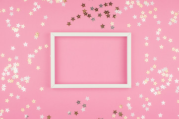 White picture frame and sequins stars on pink background. Top view, flat lay. Mockup for party or birthday invitation.