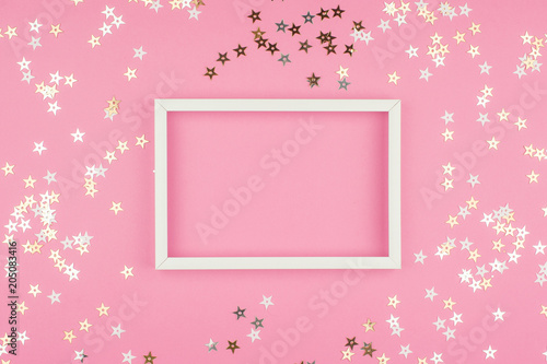 White picture frame and sequins stars on pink background. Top view, flat lay. Mockup for party or birthday invitation.