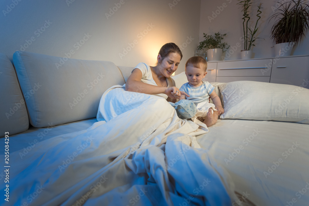 Fototapeta premium Young mother lying with her baby son in bed and giving him plush toy
