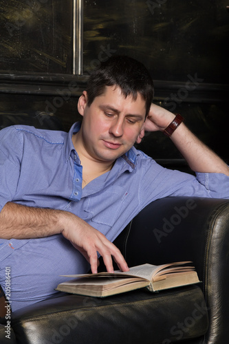Young man is lying on the sofa and is reading a book. Close-up.