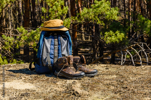 Backpack, touristic boots and hat on a ground in a coniferous forest