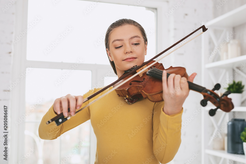 Keep attention. Delighted girl keeping smile on her face while looking at her instrument Keep attention. Delighted girl keeping smile on her face while looking at her instrument