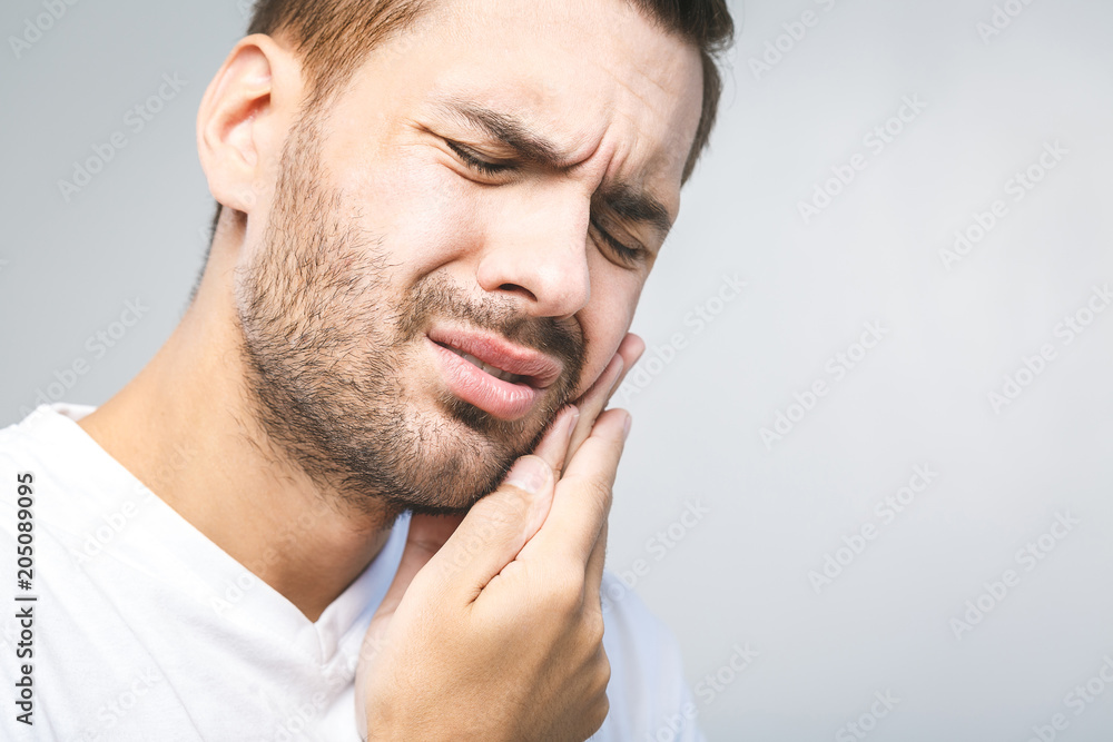Toothache. Handsome young man suffering from toothache, closeup, touching his cheek to stop pain against white background. Strong toothache Toothache. Handsome young man suffering from toothache, closeup, touching his cheek to stop pain against white background. Strong toothache