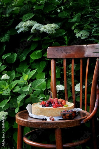 In a green garden in the nature fruit pie with strawberries and other berries. On an old vintage wooden chair