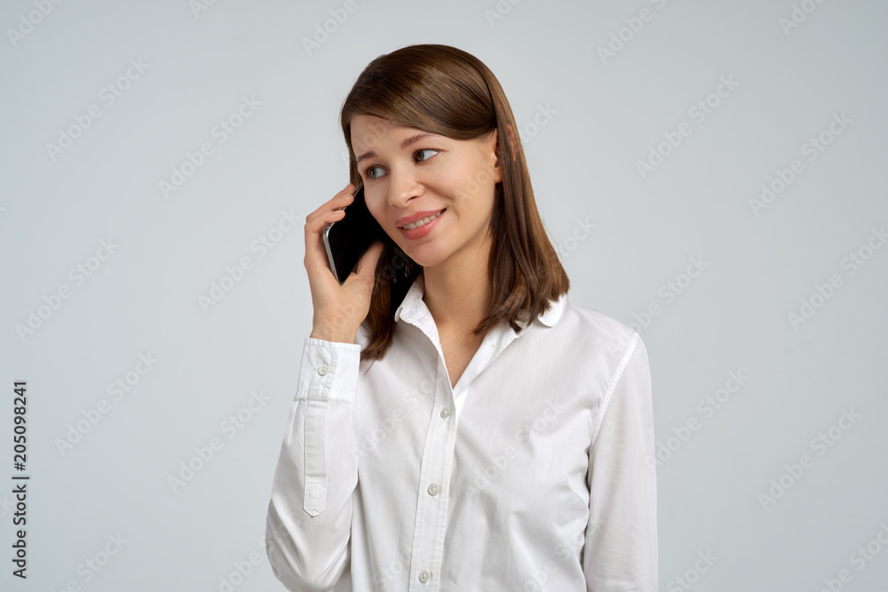 attractive young brunette woman in white blouse shirt talking on mobile phone and smiling. Studio portrait on isolated background attractive young brunette woman in white blouse shirt talking on mobile phone and smiling. Studio portrait on isolated background