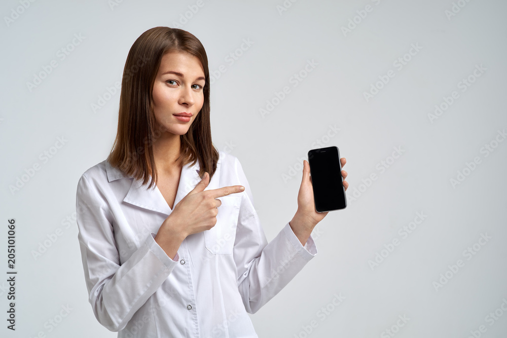 Studio portrait of young attractive female doctor in white medical robe holding smartphone in hand and finger licking on display Studio portrait of young attractive female doctor in white medical robe holding smartphone in hand and finger licking on display