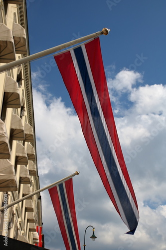 Narodowe flagi Norwegii zawieszone na ścianie budynku, na ulicy, na zewnątrz, dekorują miasto podczas narodowego święta, na tle niebieskiego nieba z białymi malowniczymi chmurami