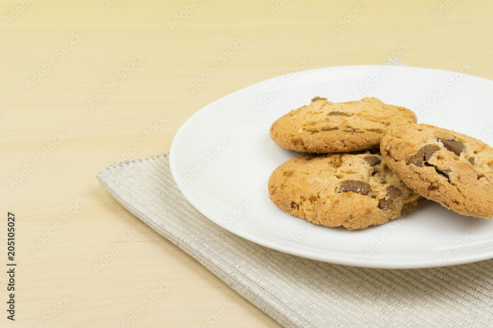 three pieces of chocolate chip cookies in a white round dish on the wooden table. three pieces of chocolate chip cookies in a white round dish on the wooden table.