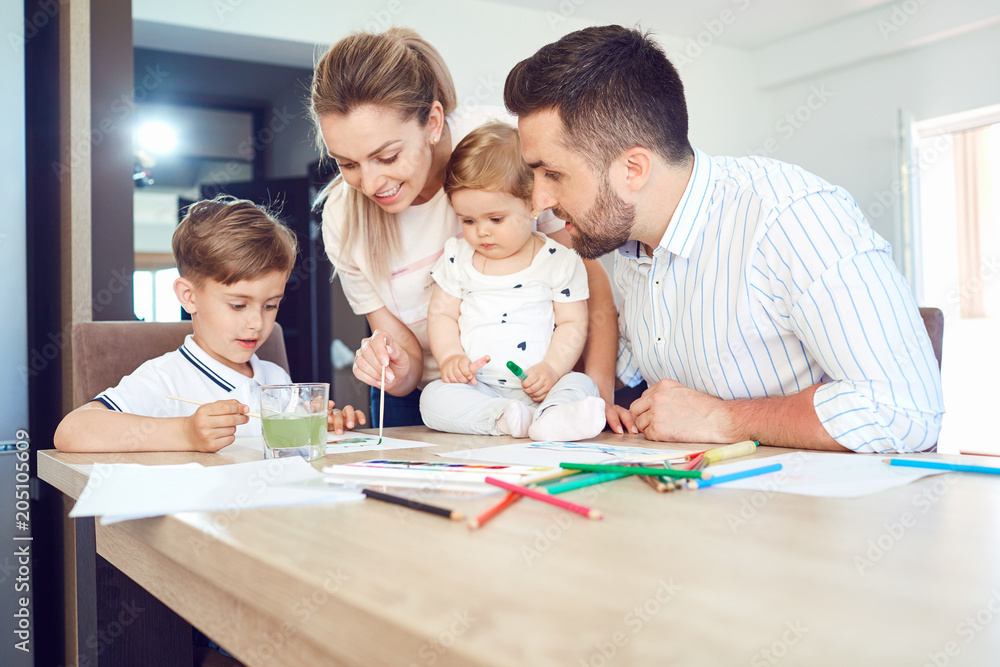 Happy family draws paints on a paper at the table in the room. Happy family draws paints on a paper at the table in the room.