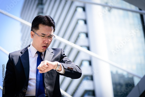 The asian businessman has holding a black bag and looking on watch in hurrying time.