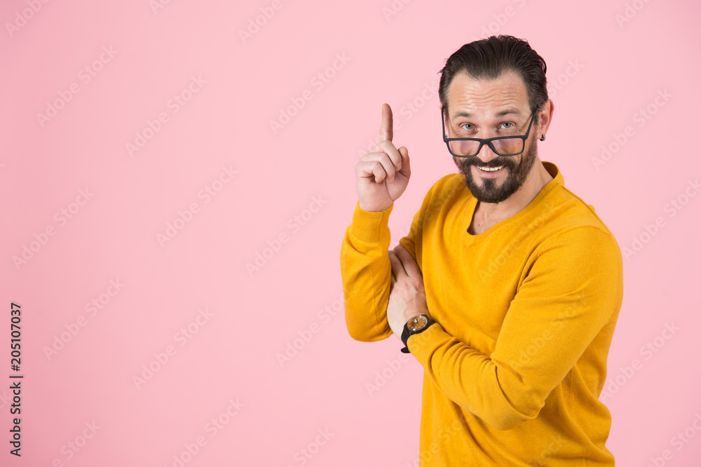 Smiled and happy bearded fashion man pointing up with glasses on nose. Man get the idea isolated in studio on pastel pink background!. Smiled and happy bearded fashion man pointing up with glasses on nose. Man get the idea isolated in studio on pastel pink background!.