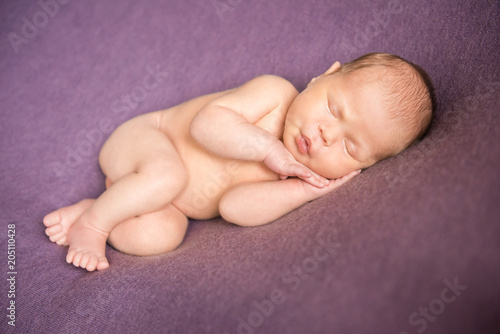 Naked newborn baby sleeping on purple background