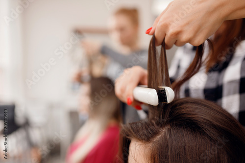 Hairdresser woman straightens her hair and makes styling, close-up of curling iron in salon