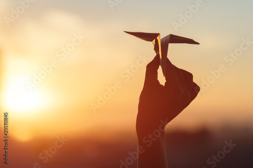 A girl is launching a paper airplane from a window at sunset.