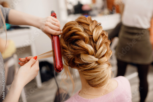 Woman hairdresser making hairstyle to blonde girl in beauty salon. photo