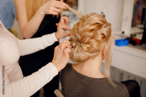 Hairdresser woman conducts training for pupil in salon, weaving braid hair, wedding styling.