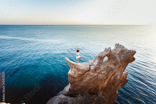 Yoga on the beach. A beautiful woman in white with a perfect body is practicing yoga at the top of a cliff. Healthy lifestyle. Extreme journey.