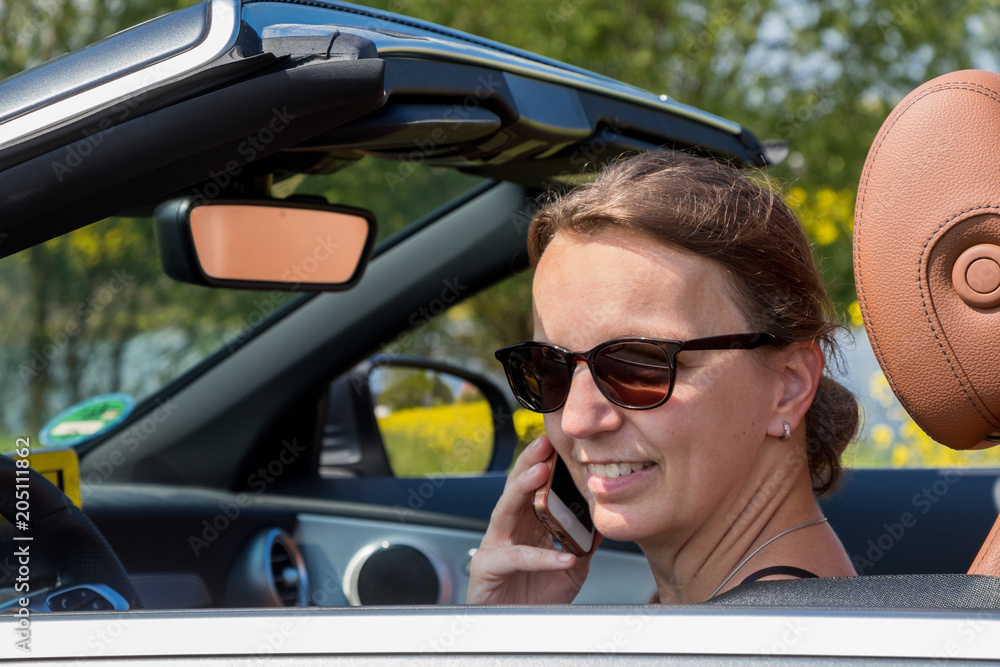 Portrait of attractive brunette woman driver using smart phone while driving in a luxury convertible car
Portrait of attractive brunette woman driver using smart phone while driving in a luxury convertible car