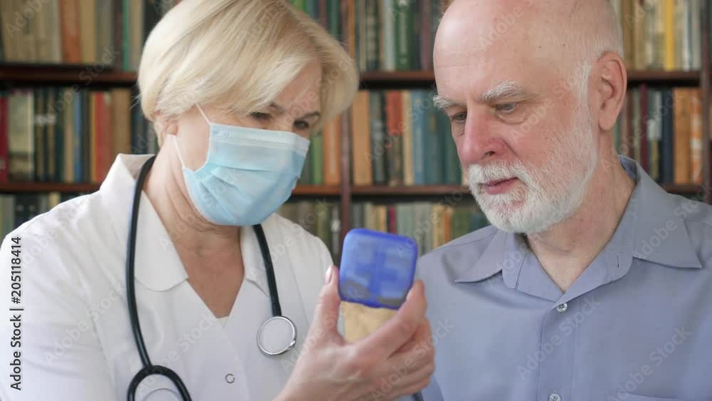 Female professional doctor in medical mask with stethoscope at work. Senior woman physician talking to sick senior male patient at home consulting about new drug. Showing case of pills capsules Female professional doctor in medical mask with stethoscope at work. Senior woman physician talking to sick senior male patient at home consulting about new drug. Showing case of pills capsules