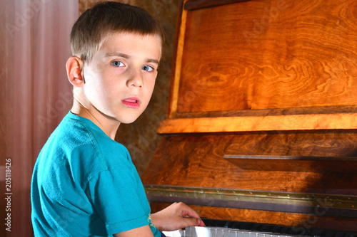 The boy plays the guitar near the piano and looks thoughtfully photo