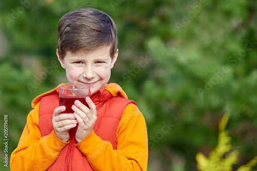 Cute smiling Caucasian boy with a glass of juice outdoors.