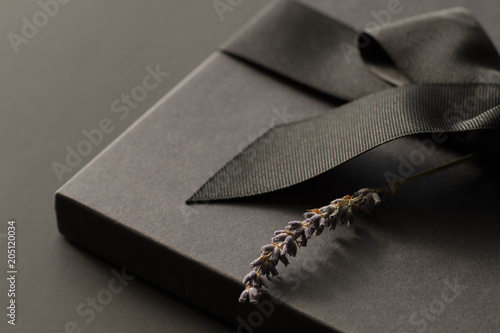Black gift box on a dark contrasted background, decorated with a textured bow and feathers, creating a romantic atmosphere. Typically used for birthday, anniversary presents, gift cards, post cards.