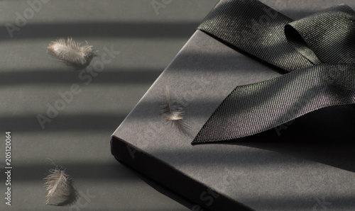 Black gift box on a dark contrasted background, decorated with a textured bow and feathers, creating a romantic atmosphere. Typically used for birthday, anniversary presents, gift cards, post cards.